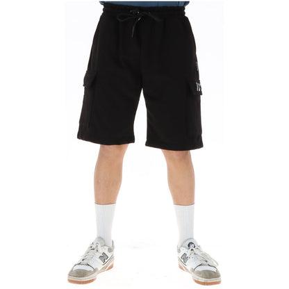 Image 1 : Bermuda cargo Icon homme noir en molleton, poches latérales à rabat et cordon de serrage, porté avec baskets New Balance blanches — Delvale